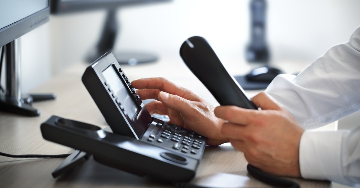 Close-up to the hands of a man wearing a white shirt, holding the handset while pressing a button next to the screen.