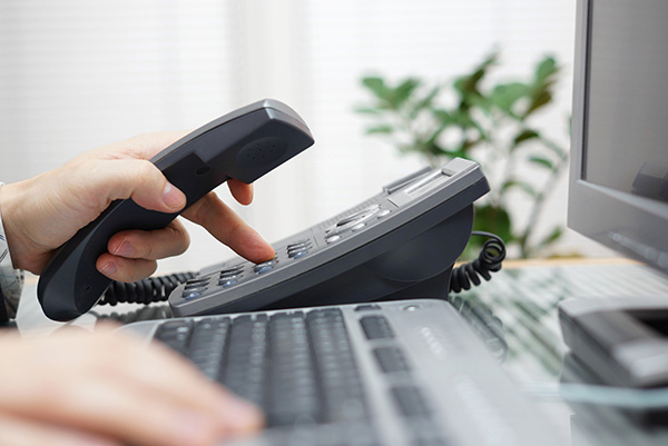 person dialing on a nortel pbx phone sitting on a desk next to a computer