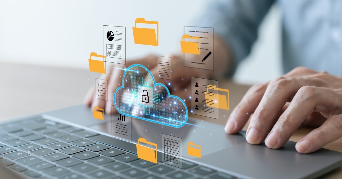 Someone's hands resting on a laptop, using the keypad. There is an overlayed image of different files, a cloud, and a secure lock.
