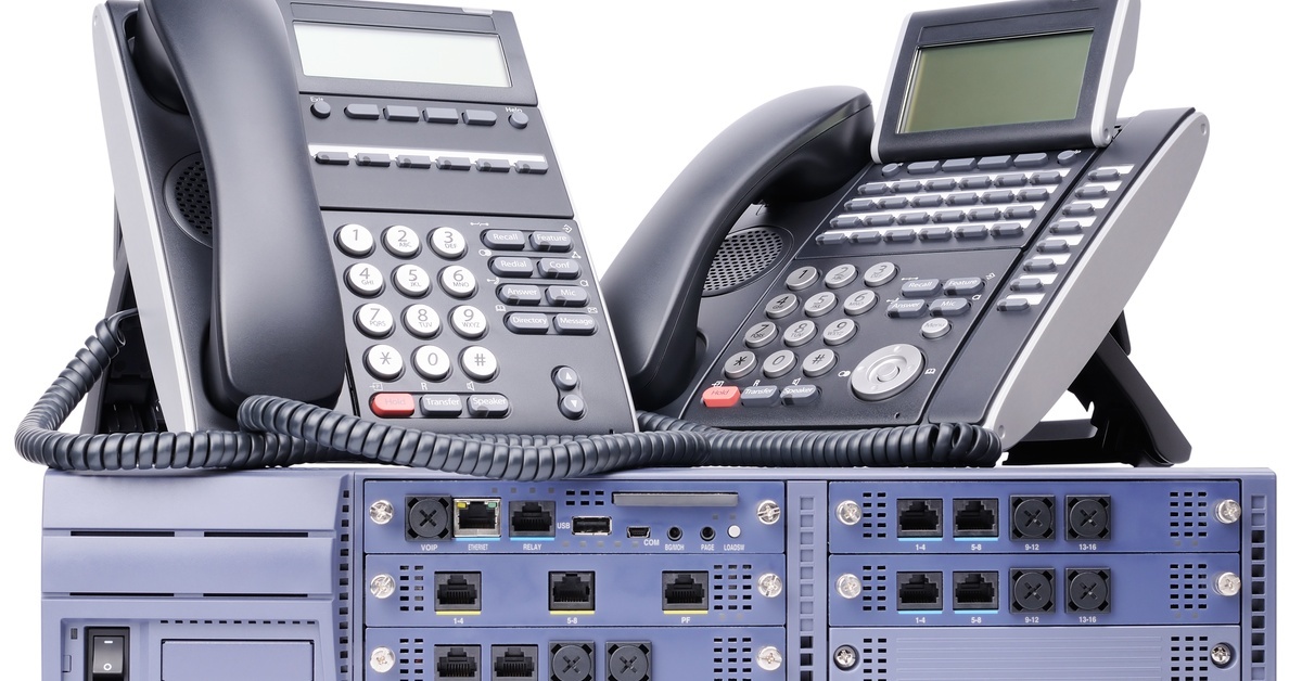 Two black, corded handset phones sitting on top of a unit with many different types of ports.