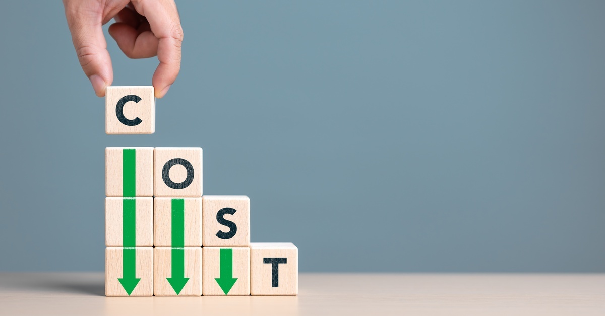 A stack of light wood blocks spelling out "cost" with down arrows on them. A hand places the "C" block on top of the stack.