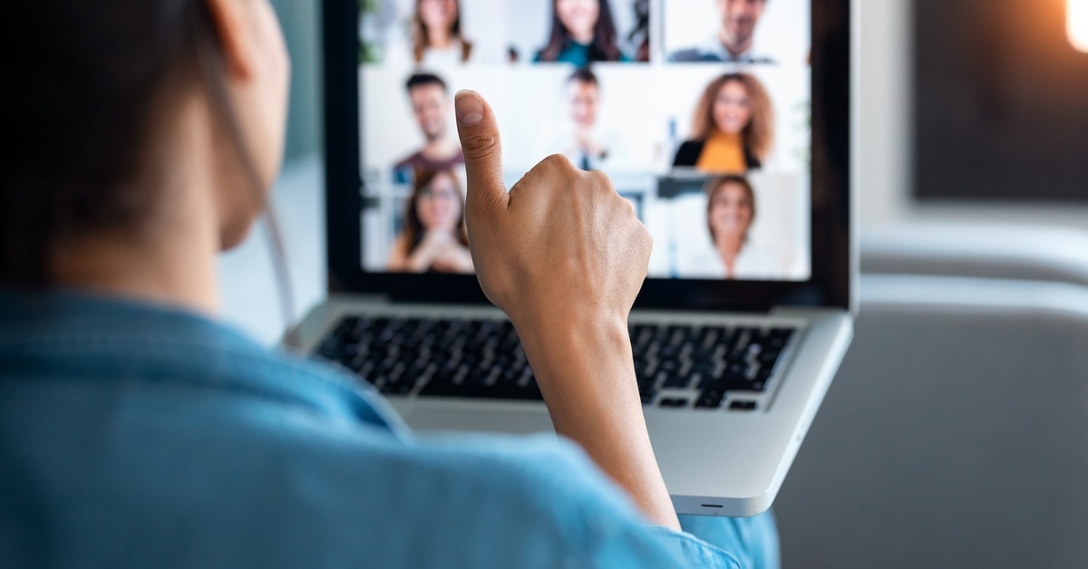A woman looking at a laptop showing different face cams in a video call. She is giving a thumbs up to the laptop.