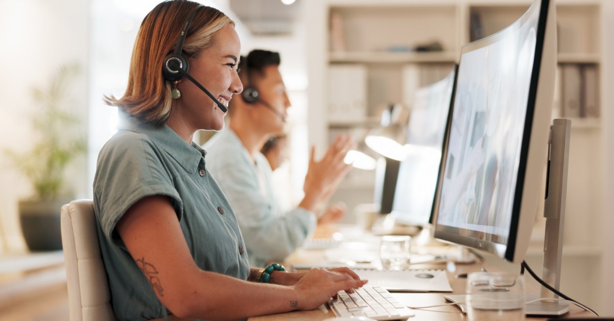 A row of people at a table, each with their own headset and computer. The woman in front is smiling while on a call.