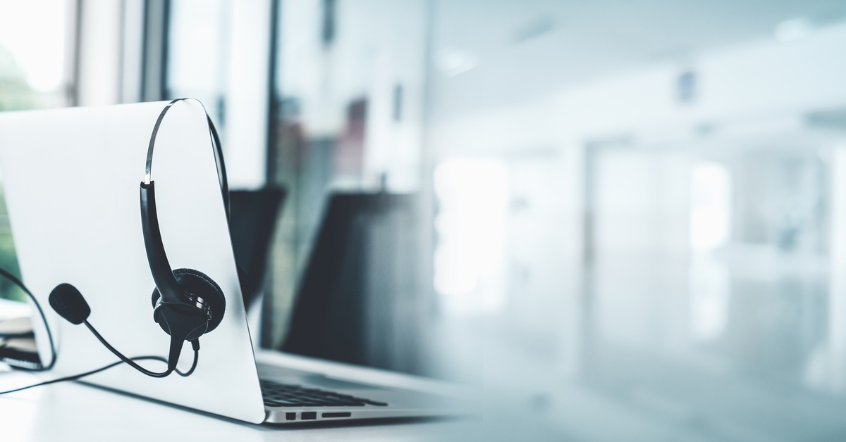 A laptop with a headset hanging over the screen. The laptop is sitting on a white table in an office.